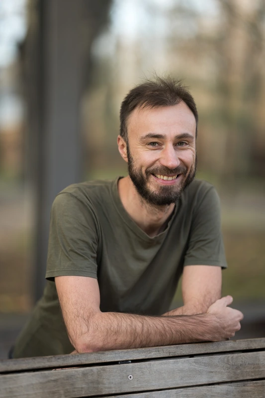 Portrét usmívajícího se Tomáše v olivově zeleném tričku, opřený o lavičku
