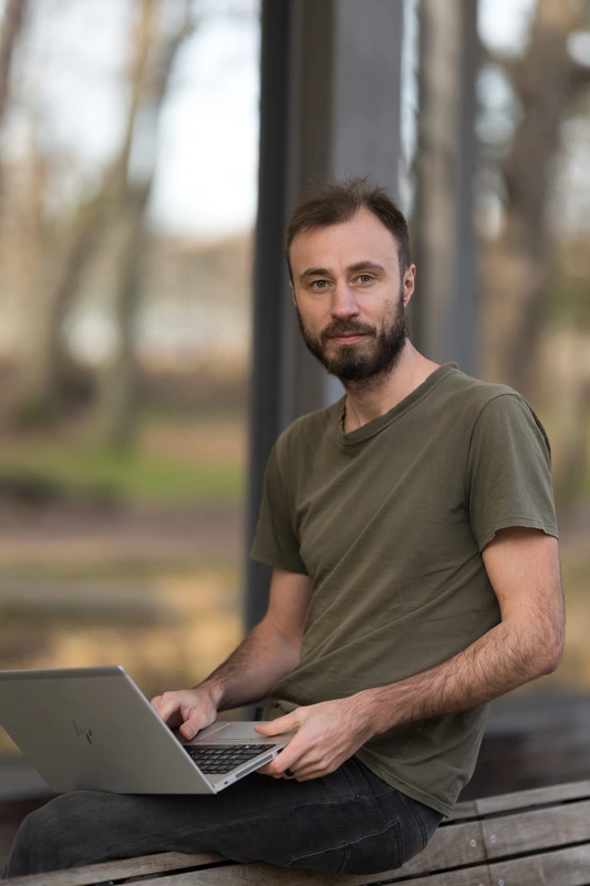 Tomáš Shejbal pracující na notebooku venku, sedí na dřevěné lavičce"