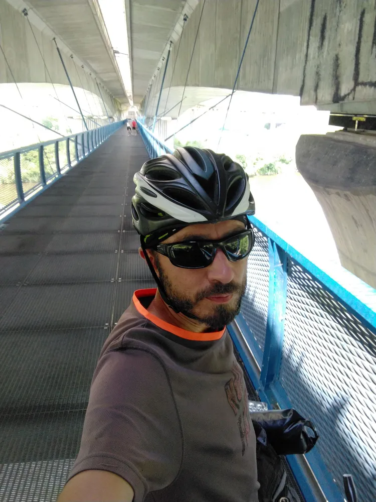 Koloběžkař v helmě a slunečních brýlích pořizuje selfie na cyklostezce pod mostem