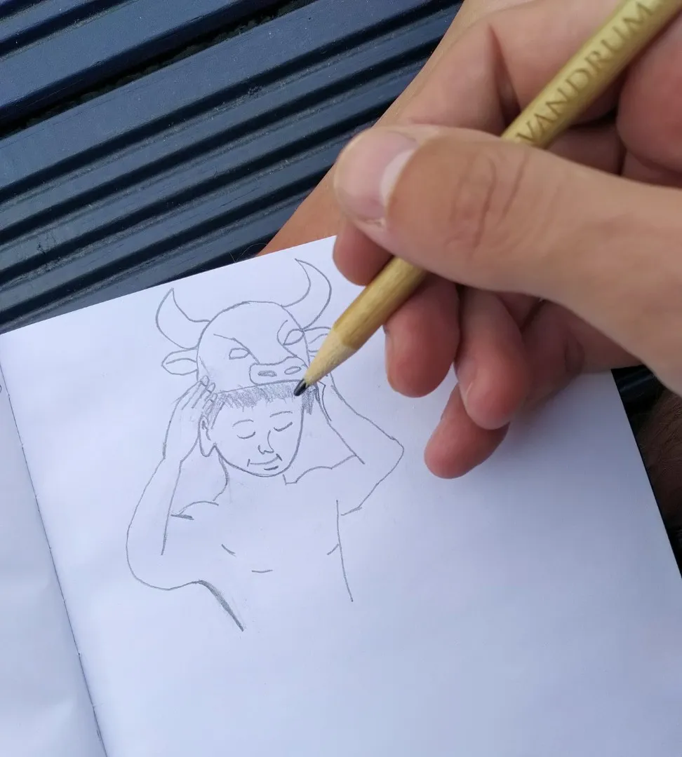 Ruka kreslící tužkou skicu postavy s býčí maskou na hlavě v náčrtníku
