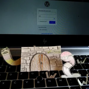 Vystřižené kreslené postavičky červů a papírová brána s nápisem "WordPressovi" stojí na klávesnici před přihlašovací obrazovkou WordPressu