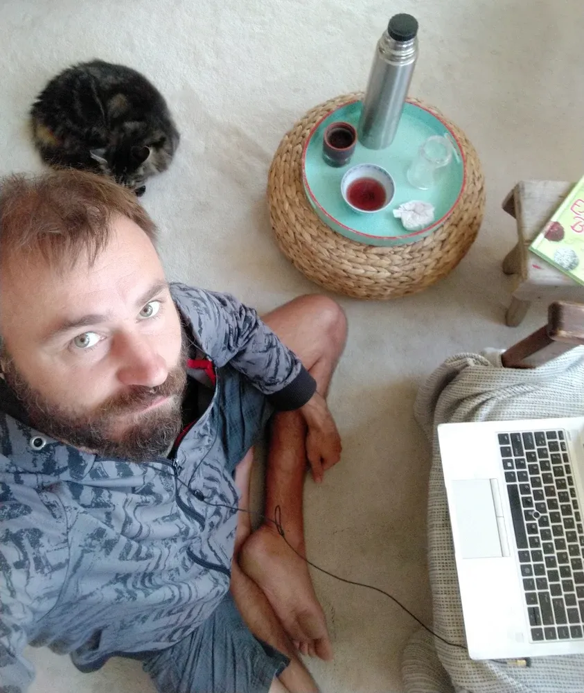 Tomáš Shejbal sedí na podlaze vedle kočky, termosky s čajem a notebooku, fotí se shora
